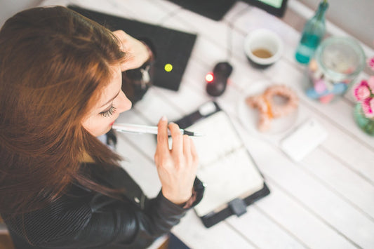 Woman holding pen near her mouth as she thinks about what to write for work.