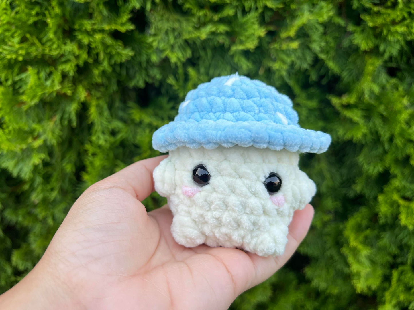 Blue crochet mushroom sitting looking forward in a garden.